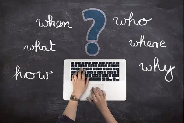 A laptop keyboard sitting on a chalkboard that says When, Who, What, Where, How, Why.
